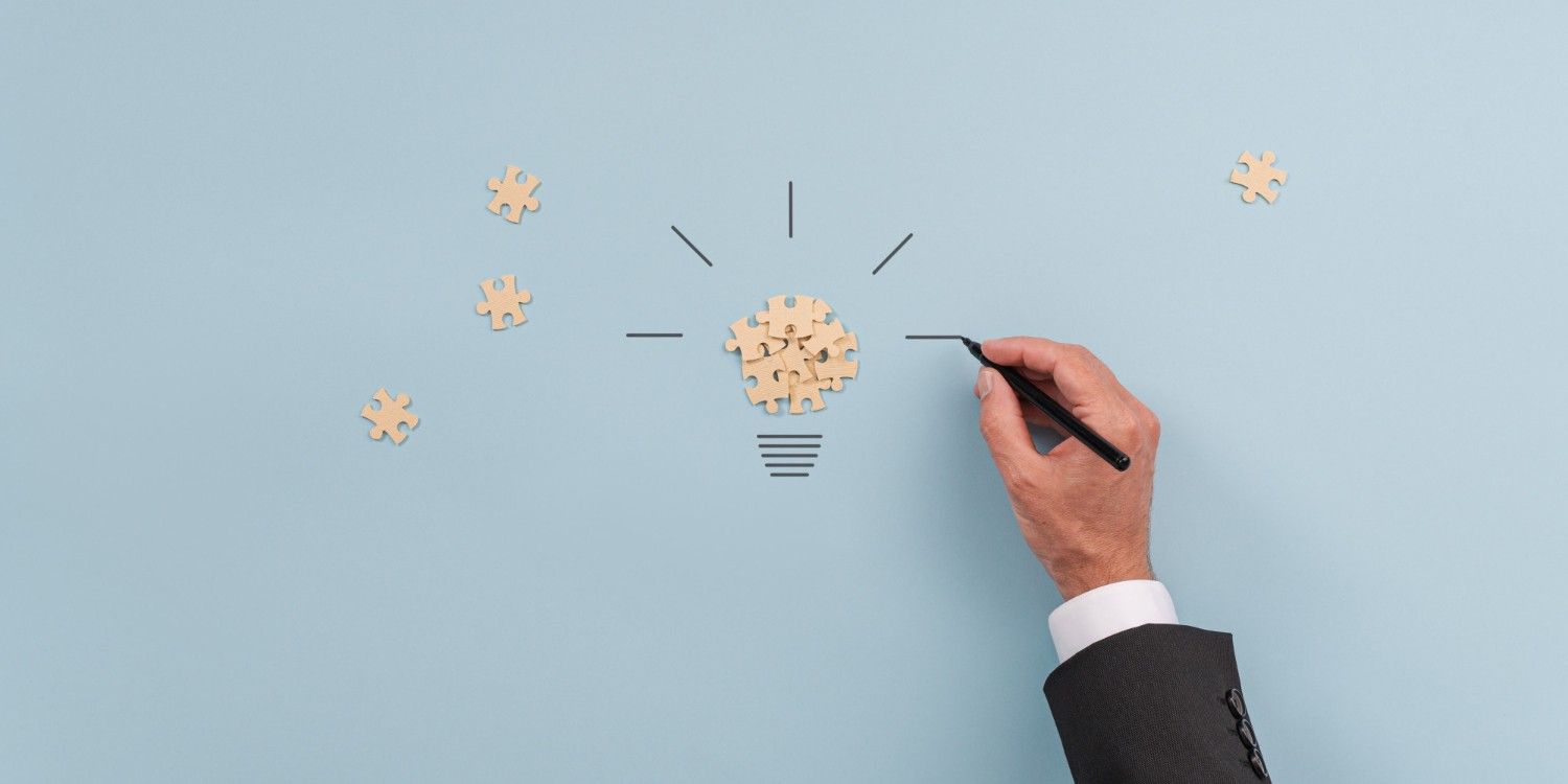 Ręka osoby rysującej na kartce, na kartce puzzle ułożone w kształt żarówki