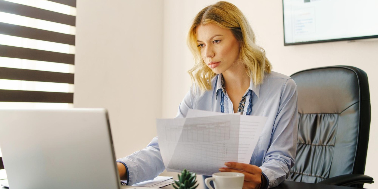 Kobieta pracująca przy komputerze, w ręku trzyma dokumenty