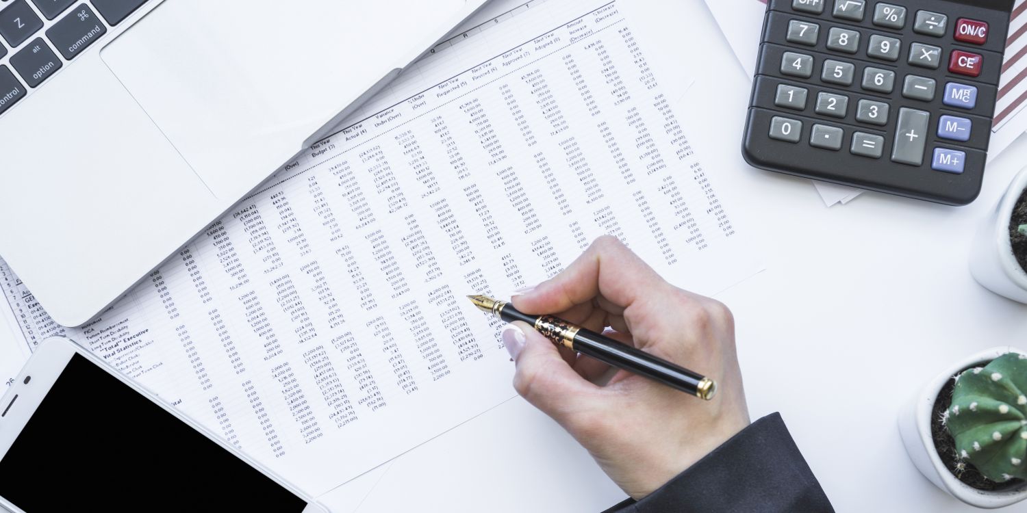 Ręka z piórem atramentowym nad biurkiem, na biurku dokumenty i kalkulator