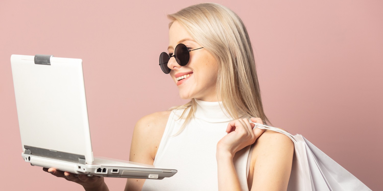 Kobieta w okularach przeciwsłonecznych trzymająca otwartego laptopa i torbę na zakupy