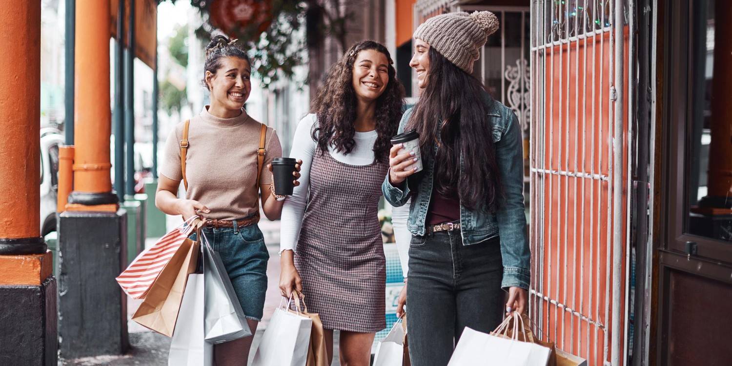 Trzy uśmiechnięte kobiety idące z torebkami zakupowymi pasażem