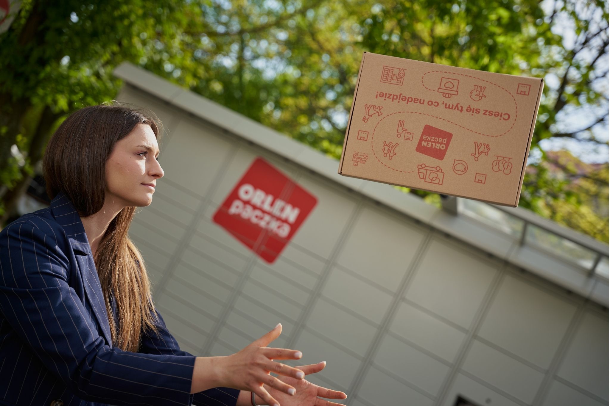Kobieta podrzucająca paczkę na tle paczkomatu ORLEN