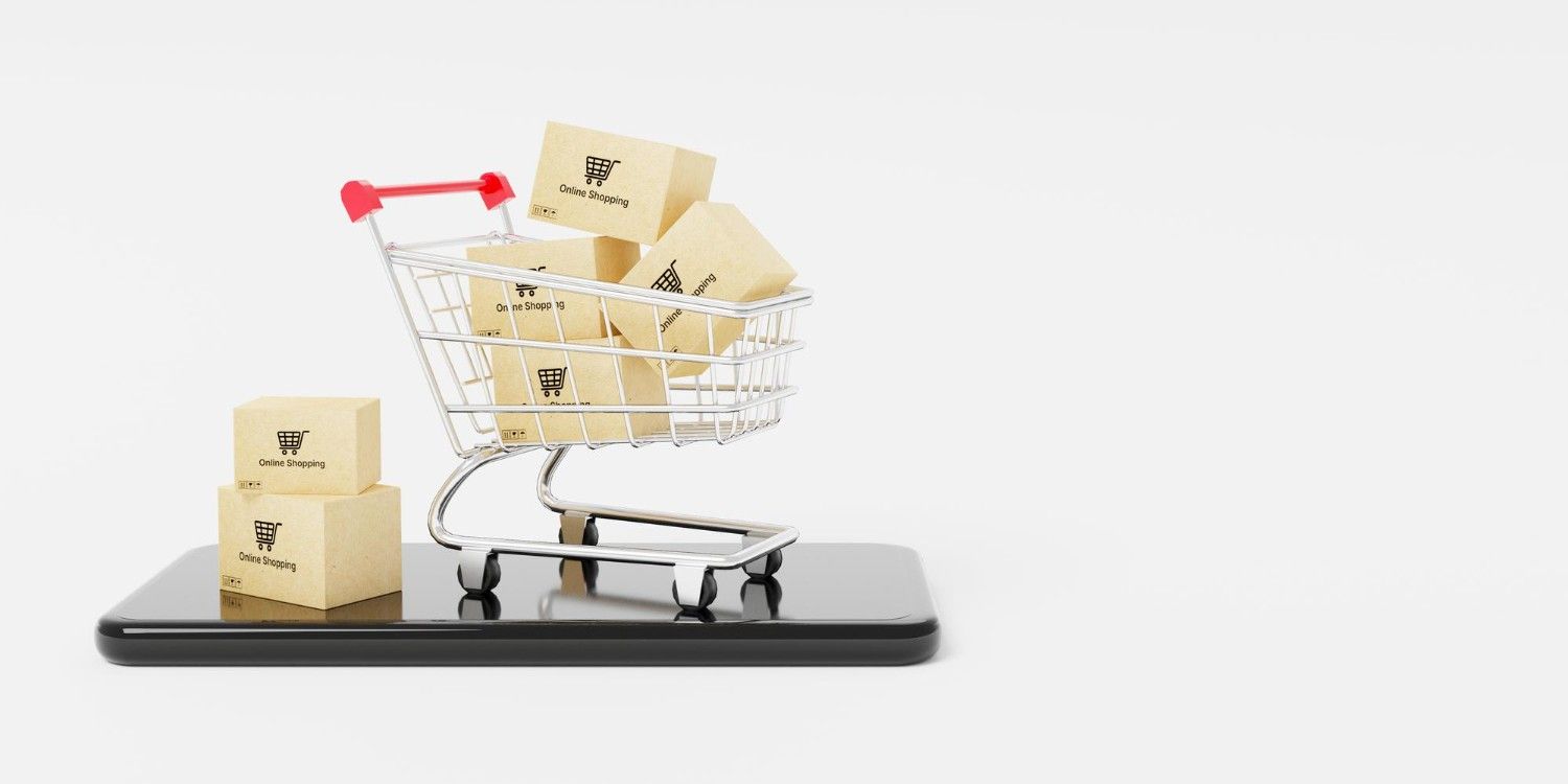 Koszyk zakupowy z paczkami w środku stojący na telefonie, obok koszyka dwie małe paczki