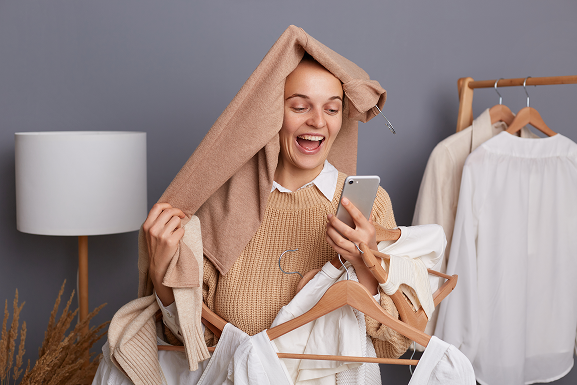 szczęśliwa kobieta trzymająca telefon w ręku oraz kilka ubrań